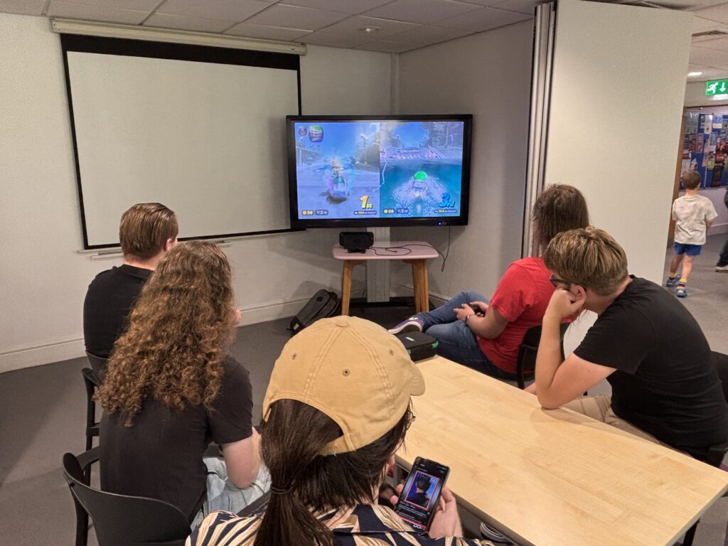 A group of members gathered round a TV playing Mario Kart